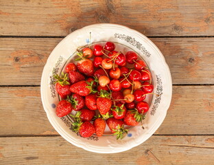 Plate with ripe strawberries and cherries on  background of  boardwalk