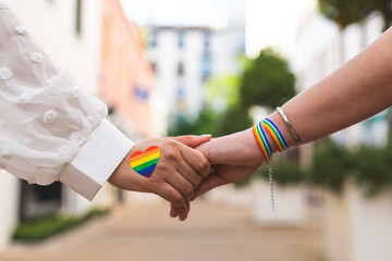 Fototapeta premium Close Up of Lesbian Women Holding Hands Wearing Gay Bracelet Outdoors. LGBTQ Concept.