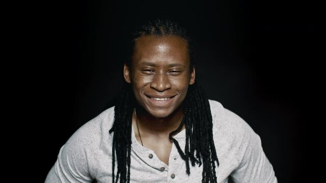 Happy african male with dreadlocks on black background. Close up of a positive young man looking at camera and smiling.

