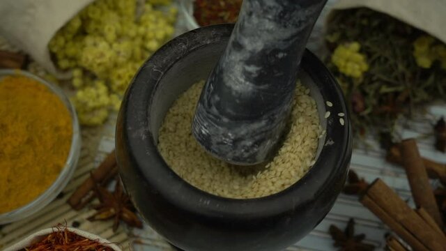Woman's hand mixes and crushes sesame seeds by granite mortar with pestle in slow motion. Healthy and organic food, herb medicine, natural care, aromatherapy and organic cosmetics concept.