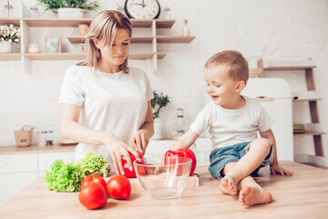 Obraz na płótnie Canvas Son with mom are cutting vegetables on salad in kitchen and have a good time together. Happy family.