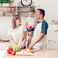 Happy family of mom, son and father are cutting vegetables on salad  and having fun together in kitchen.