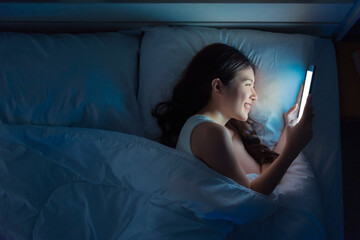 Fototapeta na wymiar Happy woman watching tv or media content in a tablet on the bed in the night