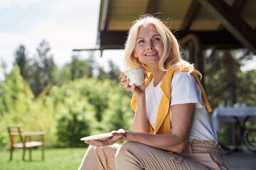 Cheerful mature woman enjoying hot drink outdoors