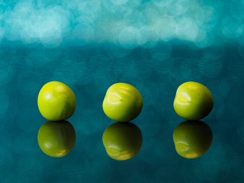 Three Green Peas On A Mirror Surface With Bokeh