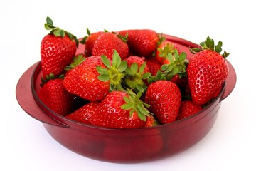 Red plastic bowl full of vibrant ripe strawberries isolated on white background