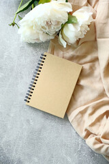 Kraft paper notebook and peony flowers on concrete stone table top view. Flat lay, top view.