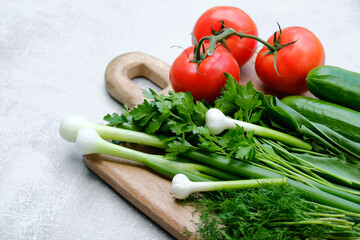Fresh ingredients of salad on cutting board. Top view organic vegetables red tomatoes, cucumbers, bunch of parsley and green onion. Dieting food, vegetarian menu concept.