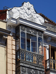 Obraz premium Revival building with metallic enclosed balcony and beautiful decorated pediment on the top. Old city center of Madrid. Spain. 