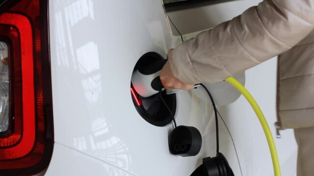 Closeup woman coming to the EV and plugging a charger connector into the electric car. Zero emission vehicle