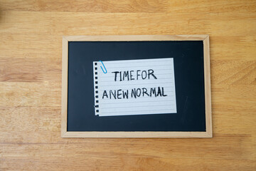 Obraz premium Conceptual hand writing showing Time For A New Normal, on white paperclip hold written chalkboard on wooden deck.