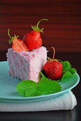 A piece of cake with strawberry cream, sprinkled with coconut shavings.Fresh strawberry.