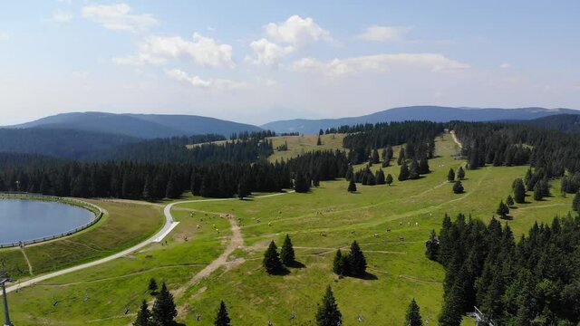 Rogla Slovenia mountain sports resort ski lift chairs below and round lake left, Aerial flyover shot