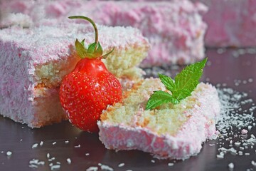 A piece of cake with strawberry cream, sprinkled with coconut shavings.Fresh strawberry.