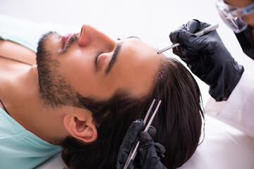 Young man visiting female beautician in hair transplantation con - obrazy, fototapety, plakaty