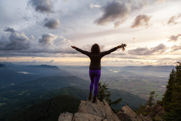 Fototapeta na wymiar Adventurous Girl on top of a Rocky Mountain overlooking the beautiful Canadian Nature Landscape during a dramatic Sunset. Taken in Chilliwack, East of Vancouver, British Columbia, Canada. Bird on Hand