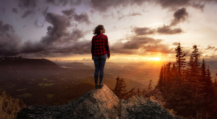 Fantasy Adventure Composite with a Girl on top of a Rock Cliff with Beautiful Nature Landscape in Background during Sunset or Sunrise. Concept: Hike, Freedom, Explore, Journey