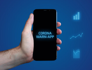 Corona Warn-App. Hand hält Telefon (Handy). Wort auf Display. Diagramme auf Hintergrund blau....