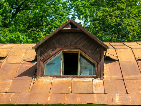 Dormer window with broken glass on the roof of an old abandoned house