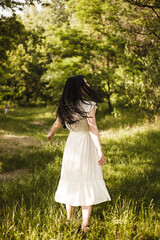 Obraz na płótnie Canvas Girl with black hair in nature. A woman in a white dress walks in nature. 