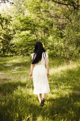 Girl with black hair in nature. A woman in a white dress walks in nature.
