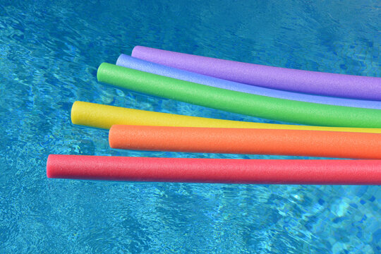 Rainbow coloured pool noodles floating in a swimming pool on a bright and sunny day.