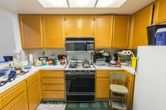 Messy condo kitchen with oak cabinets, tile countertops and piles of dishes.