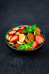 Trendy home breakfast with tiny pancakes (mini pancakes) with strawberries and mint in a bowl (cup) on a dark background. Food Background. Mini cereal pancakes.