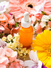 Obraz na płótnie Canvas Skin care serum in orange bottle with dropper with beautiful flowers around. Natural beauty product