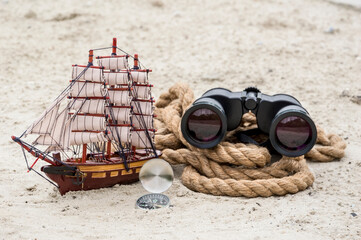 Model of an old frigate, rope, binoculars and compass on a sandy background.