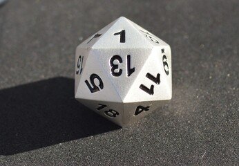 Silver metallic d20 twenty sided dice on foam surface in bright sunshine