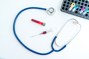 Syringe, medical stethoscope and blood tubes on table.