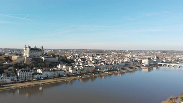 Saumur town skyline with medieval castle and church reflecting on the river at sunrise, Loire Valley, France. Aerial drone dolly shot and panning, revealing town and river bridge