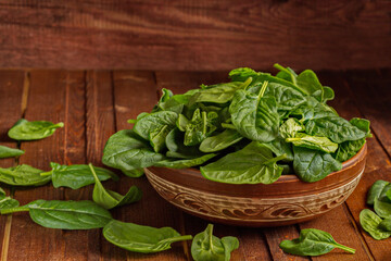 Washed fresh mini spinach in a bowl on the old wooden brown table. Selective focus. Healthy diet, vegetarian food concept. Copy space. Rustic.