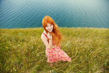 Fototapeta na wymiar romantic redhead young woman in a dress on sea coast. girl in the summer outdoors.