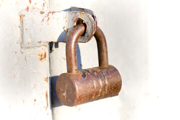 Close-up of lit by sun old rough metal padlock on garage or barn iron gate. Outdated technology,...