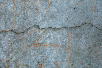 Detailed surface pattern and texture of cracked grey concrete wall with graffiti. Grunge background with copy space.