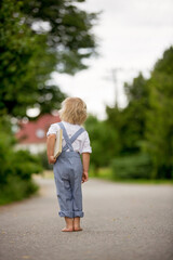 Blond toddler boy in vingate clothes holding book, standing on the street waiting for a bus