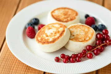 Russian Syrniki, Cottage cheese fritters or pancakes served with red currant berries, blueberries and raspberries