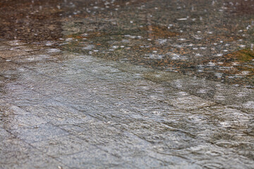 Concentric circles during the rain on the surface of the water cover the granite area of the city sidewalk.