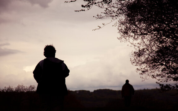 silhouette of a two mean walking away  on a path in the woods at twilight
