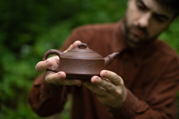 Selective focus of man holding traditional Chinese kettle outdoors 