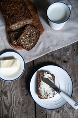 Homemade traditional Danish sourdough rye bread. Sliced bread on wooden board, cup of milk, butter and bread slice on white and blue plates on wooden background.
