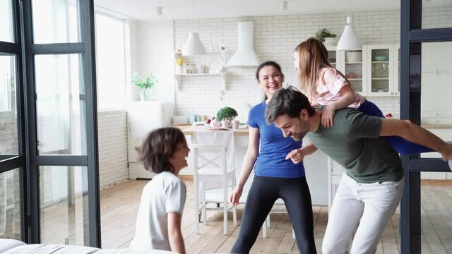 Crazy happy family, young parents and two cute little kids playing together, having fun in the living room at home. They are running and laughing, spending lovely time together