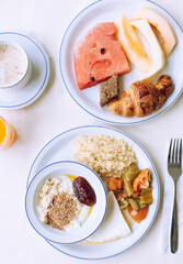 Tasty eastern hotel breakfast: plates with fruits, croissants, coffee, juice, yogurt with jam on a white table.
