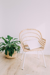 White interior with rattan wicker chair. The chair is on a wooden floor, on it lies a gray laptop. Cozy atmosphere and eco-style.