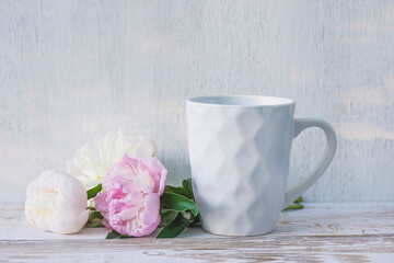 White mug of tea or coffee and bouquet of pink and white peonies on rustic white paint wooden background