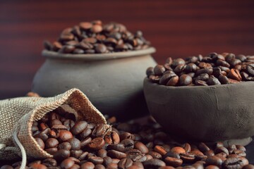 Fototapeta premium Coffee beans in an earthenware dish and a bag on a wooden table.