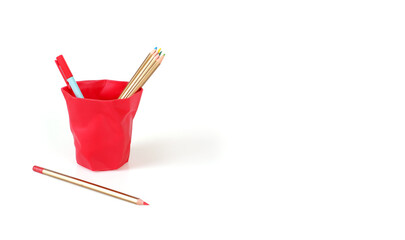 Pencils and ballpoint pen in a red plastic glass isolated on white background