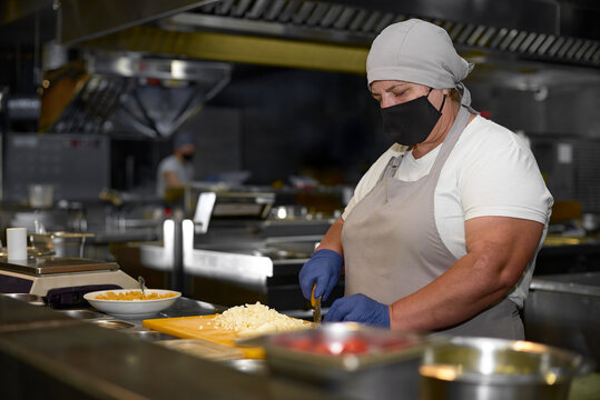 cooking, profession and people concept - woman in age chef wearing protective black mask on her face while working in restaurant kitchen